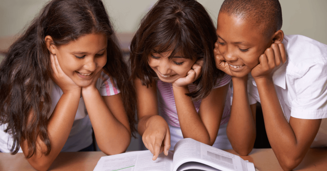 Drie basisschoolkinderen lezen samen in een boek en oefenen met het bijvoeglijk gebruikt voltooid deelwoord in de bovenbouw