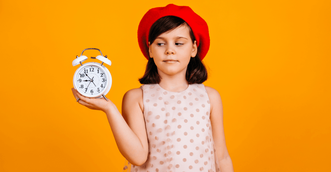 Meisje oefent klokkijken in groep 5 met een analoge wekker tegen een oranje achtergrond