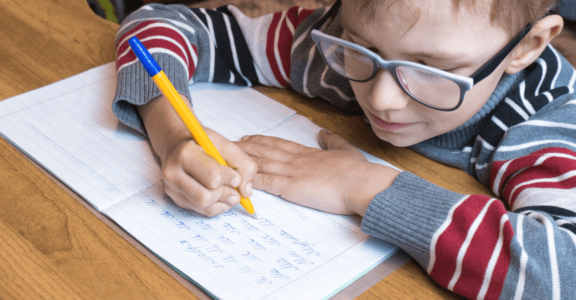 Kind op de basisschool oefent schrijfletters met potlood in een schrift.